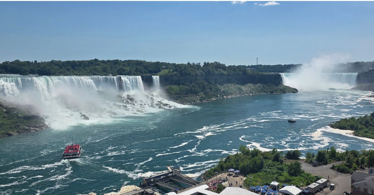 Niagara Falls American Falls Bridal Veil Falls and Horseshoe Falls American Falls and Bridal Veil Falls cascade into the Niagara River with Horseshoe Falls visible through the mist in the distance. A Maid of the Mist boat carries passengers toward the falls on a sunny summer day.