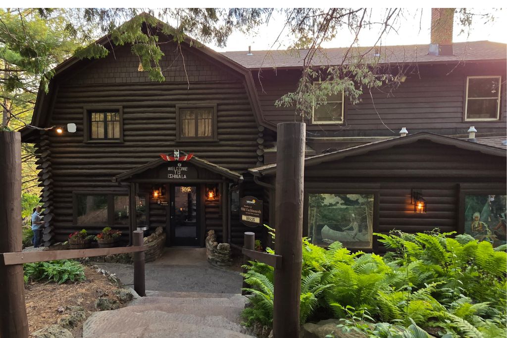 Wisconsin Dells For Adults: Beyond The Waterparks 11 Rustic log entrance to ishnala supper club surrounded by tall trees and bright green ferns in wisconsin dells.