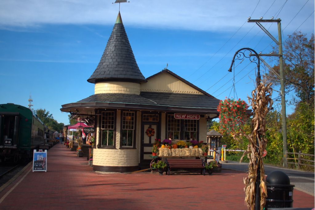 New Hope And Lambertville Fall Day Trip Guide 9 Green vintage train car sits beside the new hope railroad station with cornstalks and autumn flowers decorating the platform.