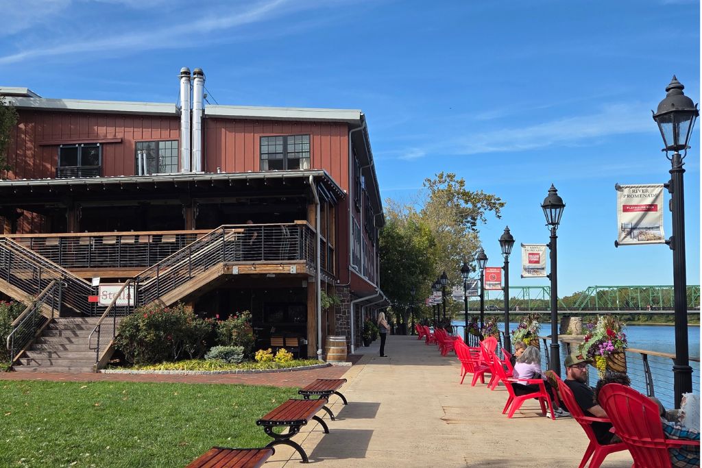 New Hope And Lambertville Fall Day Trip Guide 8 Red adirondack chairs line the new hope waterfront beside the delaware river with a green steel bridge in the background.